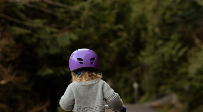 anonymous kid in helmet riding run bike on pavement in countryside